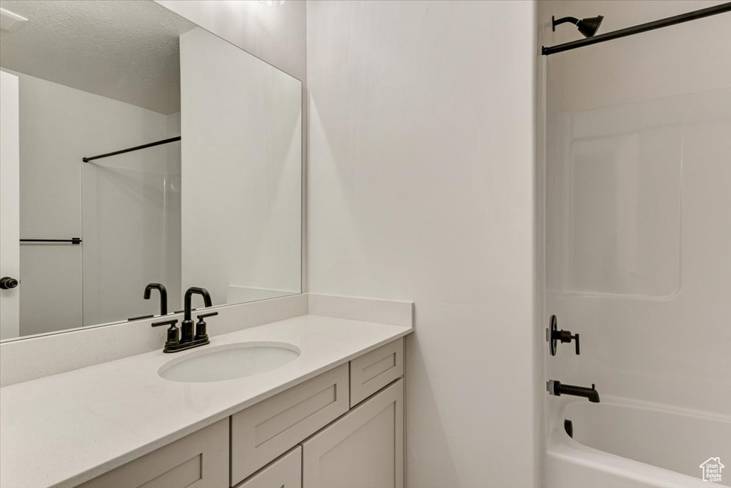 Bathroom with a textured ceiling, shower / bath combination, and large vanity