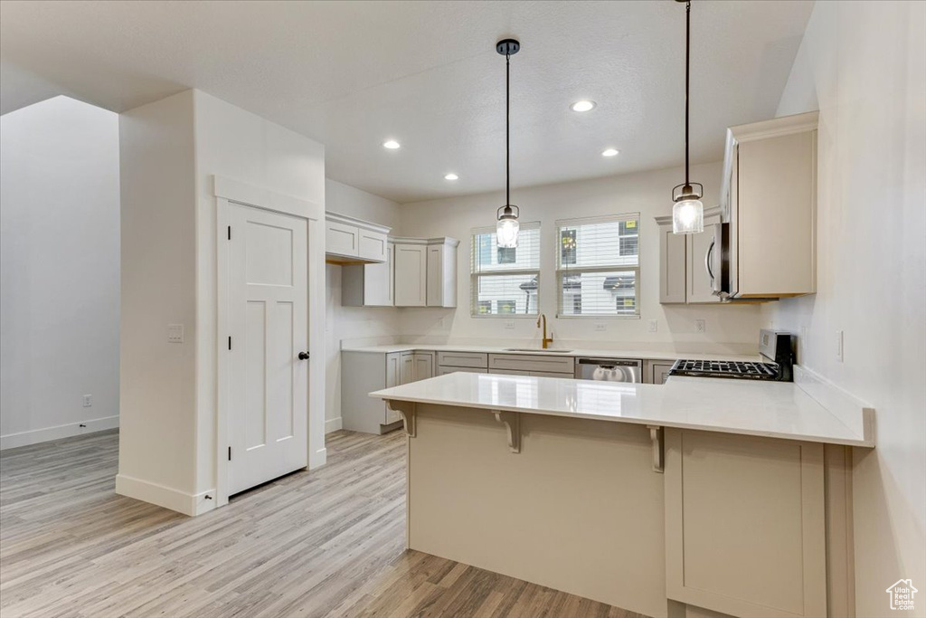 Kitchen with a kitchen breakfast bar, light hardwood / wood-style floors, pendant lighting, kitchen peninsula, and stainless steel appliances