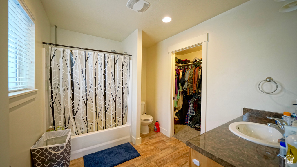Full bathroom with wood-type flooring, toilet, vanity, and shower / bath combo with shower curtain