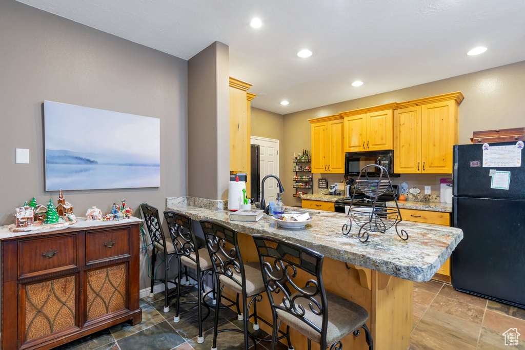 Kitchen featuring black appliances, a breakfast bar area, light tile flooring, and light stone counters