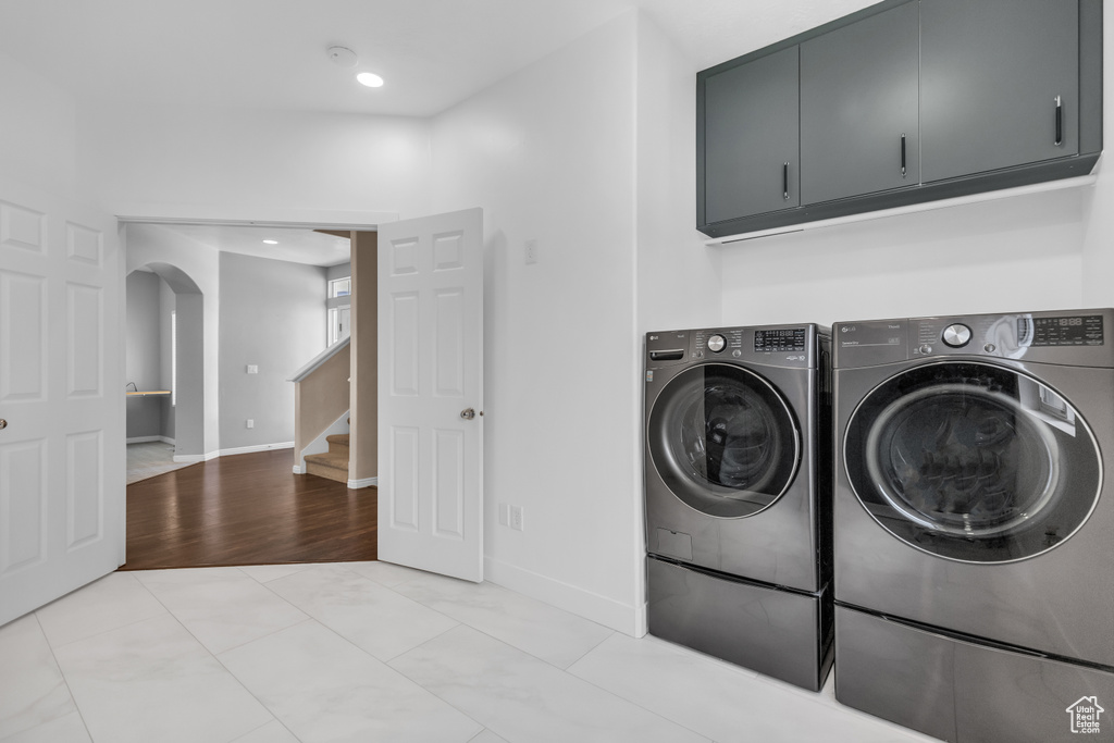 Clothes washing area with cabinets, washer and dryer, and light tile floors