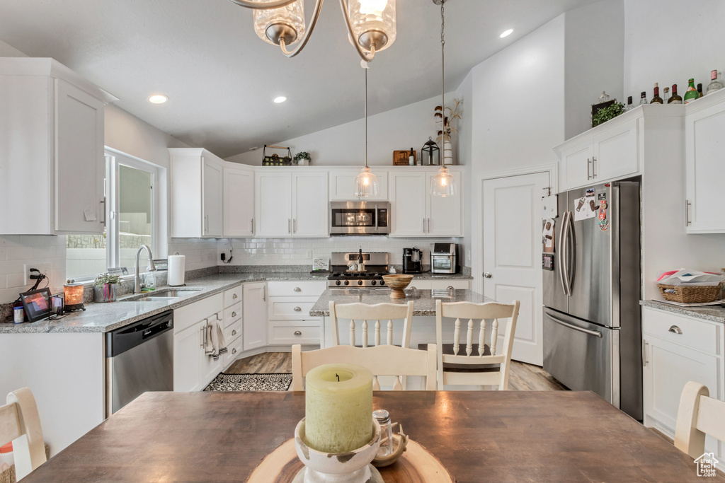 Kitchen featuring light hardwood / wood-style floors, tasteful backsplash, light stone countertops, decorative light fixtures, and stainless steel appliances