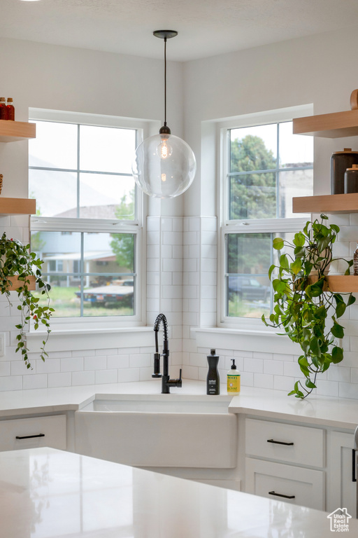 Kitchen with pendant lighting, white cabinets, sink, and backsplash