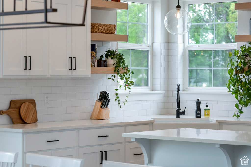 Kitchen featuring sink, white cabinetry, decorative light fixtures, and backsplash