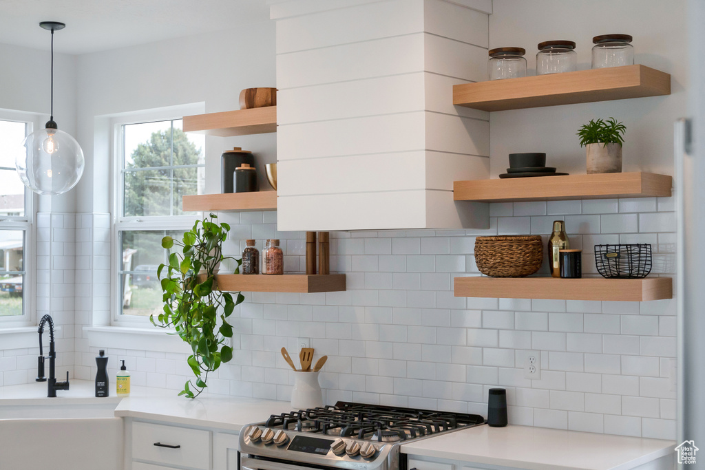 Kitchen with white cabinetry, range, decorative light fixtures, and backsplash