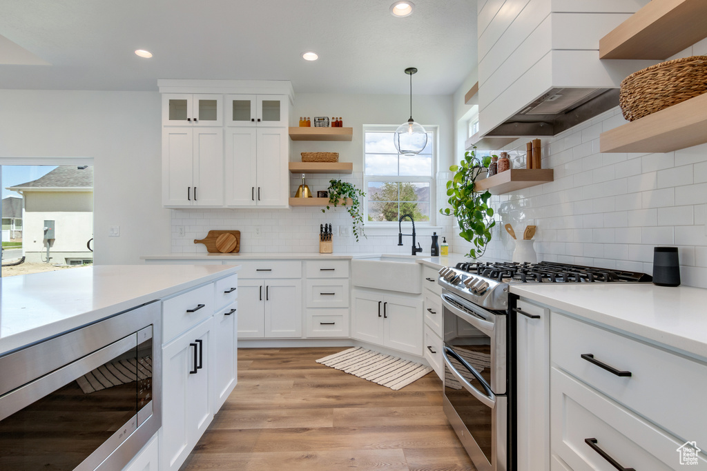 Kitchen with custom exhaust hood, pendant lighting, stainless steel appliances, light wood-type flooring, and tasteful backsplash