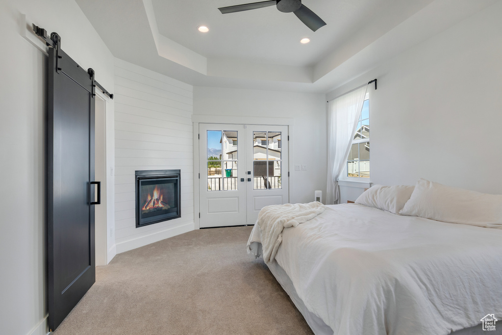 Bedroom with a barn door, light carpet, access to exterior, ceiling fan, and a raised ceiling