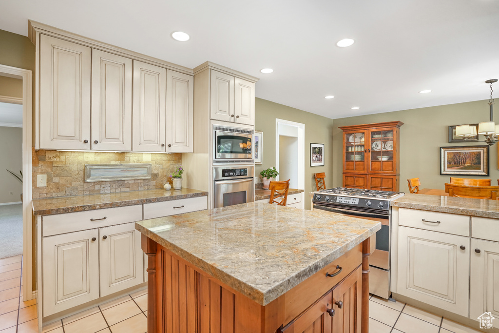 Kitchen with a center island with sink, stainless steel appliances, light tile floors, hanging light fixtures, and tasteful backsplash