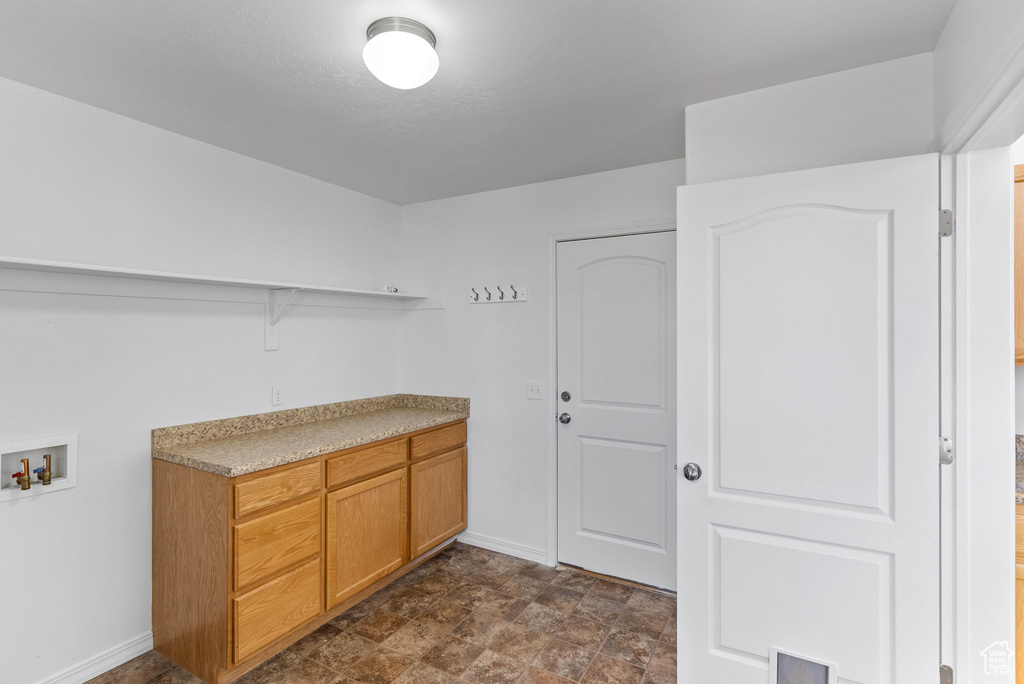 Clothes washing area featuring cabinets, hookup for a washing machine, and dark tile floors