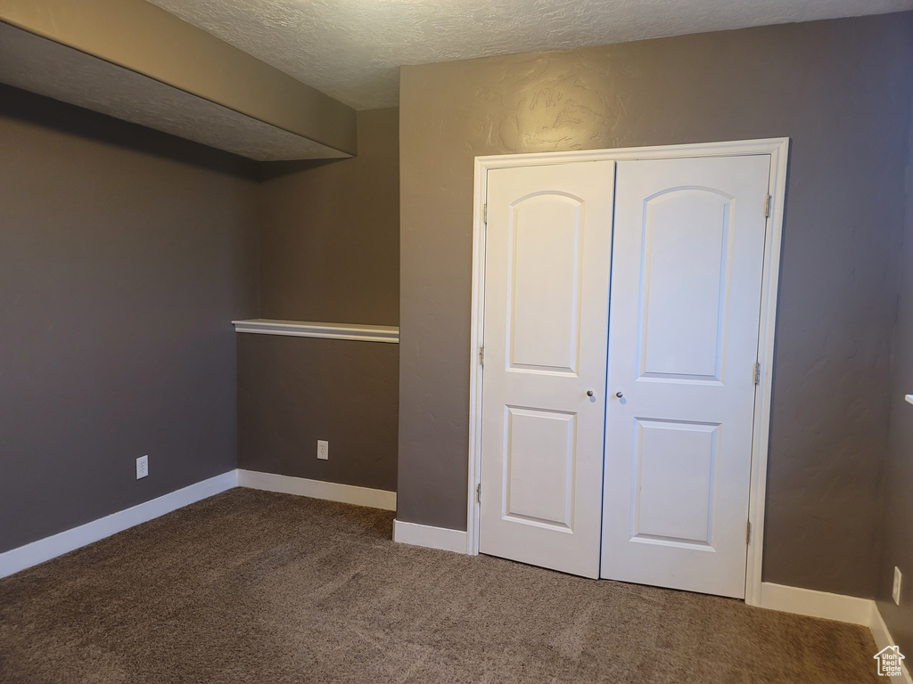 Unfurnished bedroom with a textured ceiling, a closet, and dark colored carpet