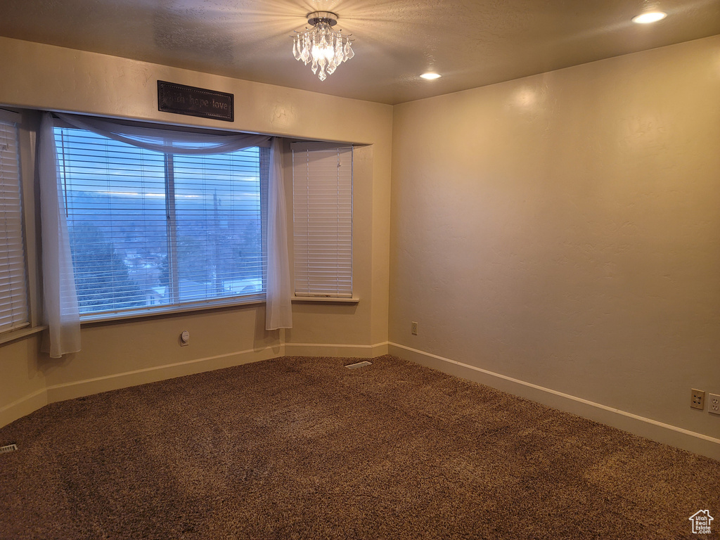 Empty room featuring a chandelier and dark colored carpet