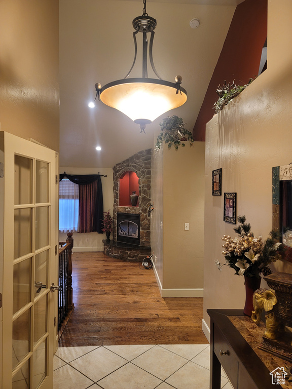 Foyer entrance featuring lofted ceiling, light wood-type flooring, a stone fireplace, and french doors