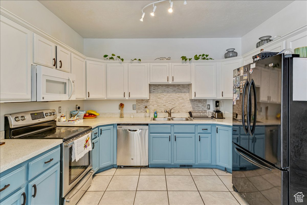Kitchen featuring appliances with stainless steel finishes, rail lighting, light tile floors, sink, and white cabinetry