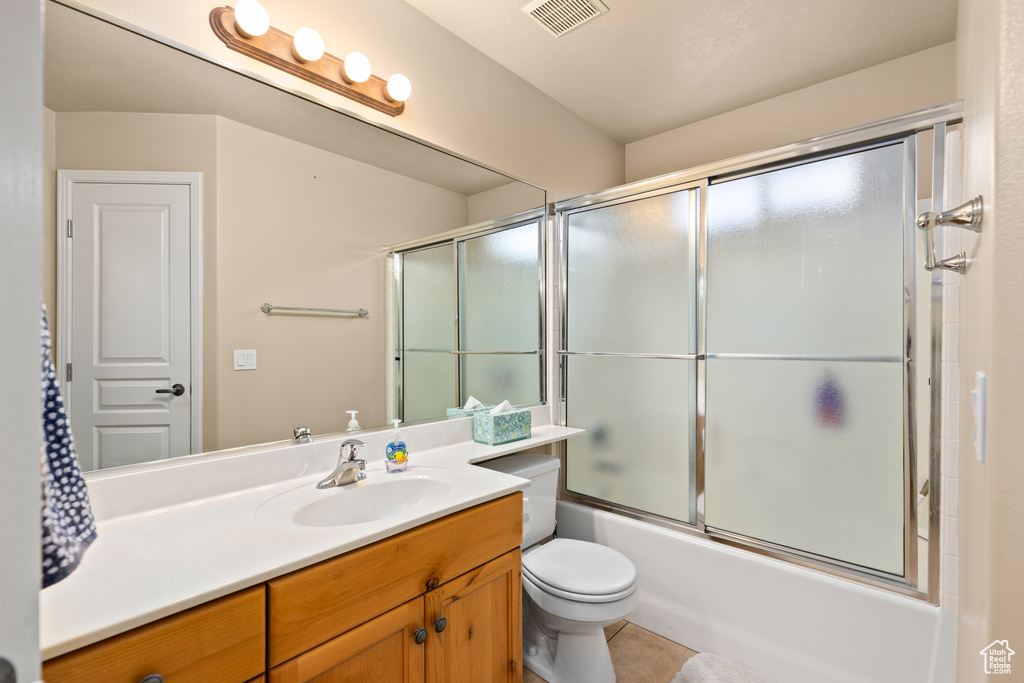 Full bathroom featuring bath / shower combo with glass door, vanity, toilet, and tile flooring