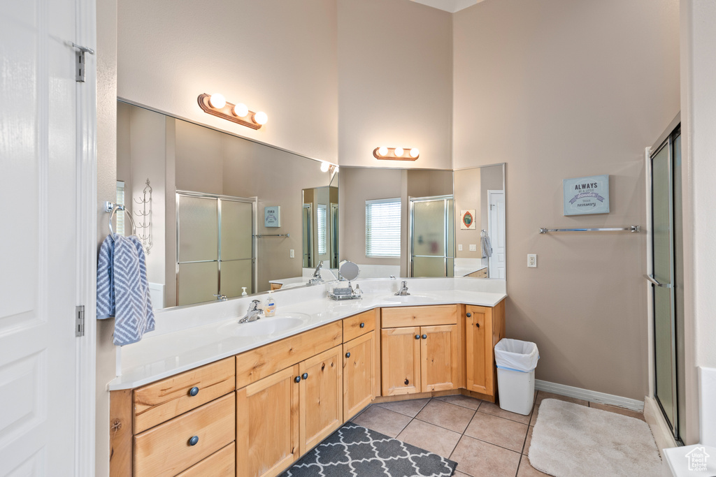 Bathroom featuring dual sinks, tile floors, vanity with extensive cabinet space, and a shower with door