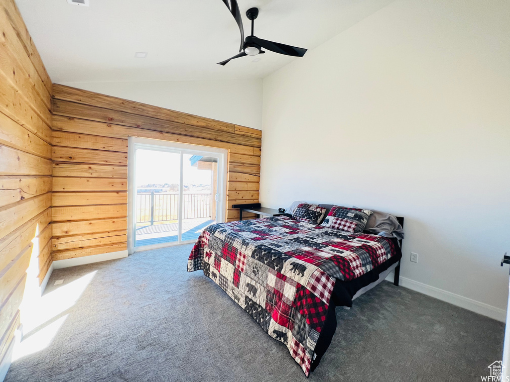 Bedroom featuring access to exterior, dark colored carpet, ceiling fan, wood walls, and high vaulted ceiling
