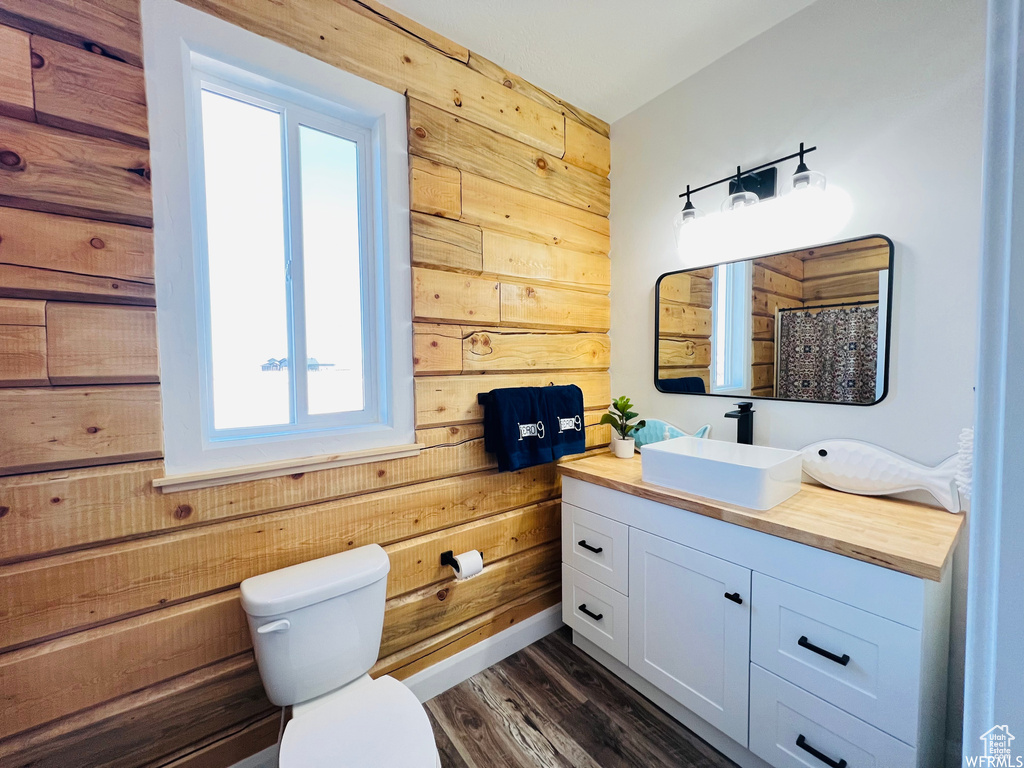 Bathroom with wood walls, hardwood / wood-style floors, toilet, and vanity with extensive cabinet space
