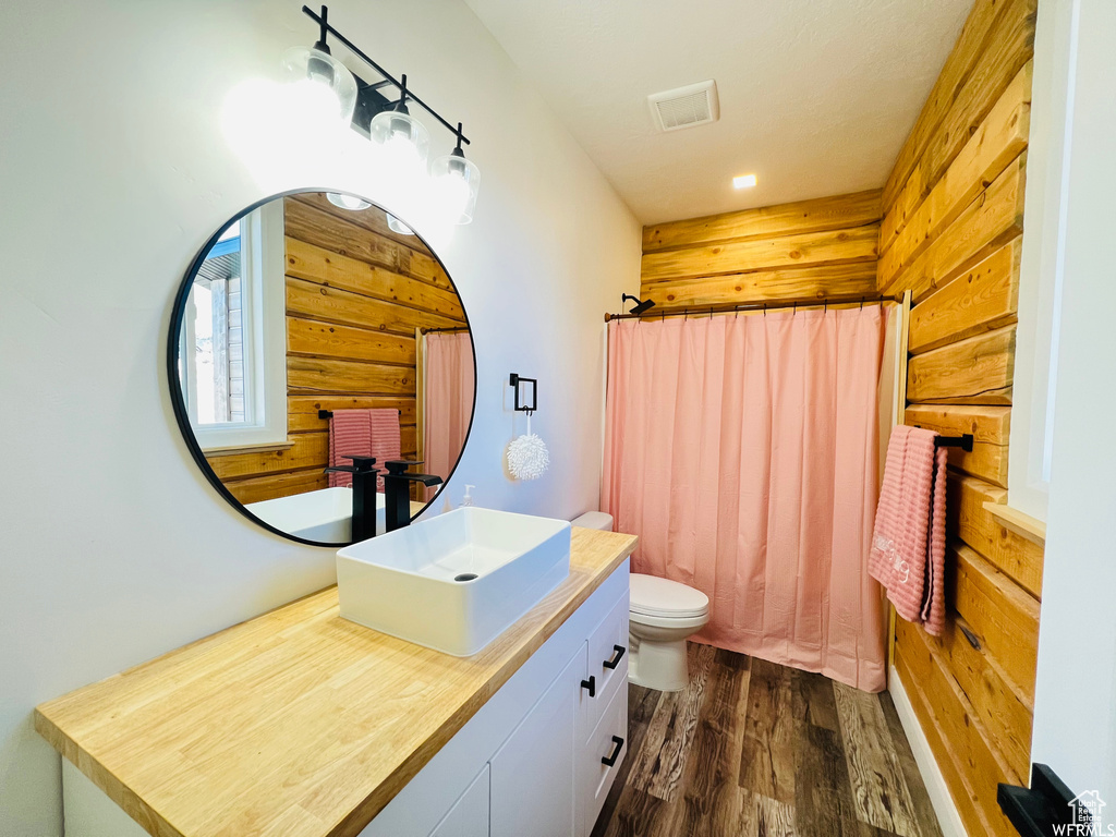 Bathroom featuring wood-type flooring, wooden walls, vanity, and toilet