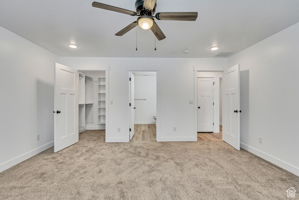 Unfurnished bedroom with ceiling fan, a spacious closet, light carpet, ensuite bathroom, and a closet