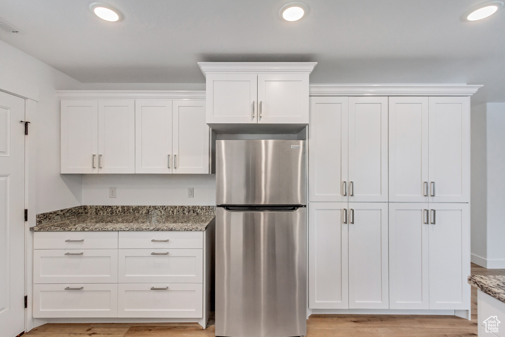 Kitchen featuring white cabinetry, stainless steel fridge, and stone countertops