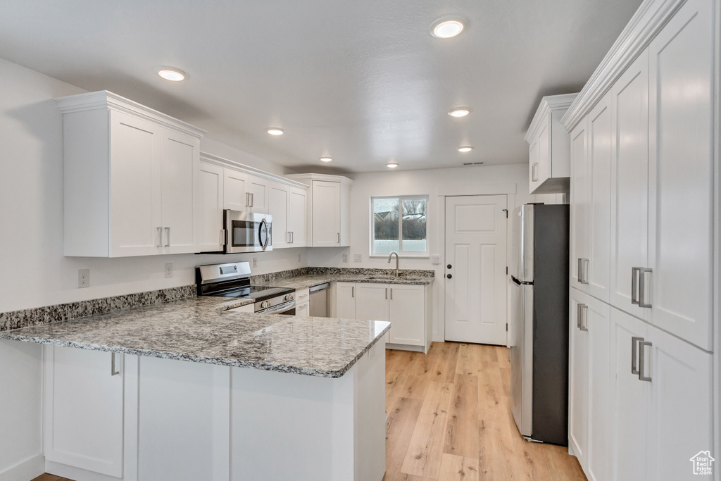 Kitchen with stainless steel appliances, white cabinets, kitchen peninsula, and light hardwood / wood-style floors