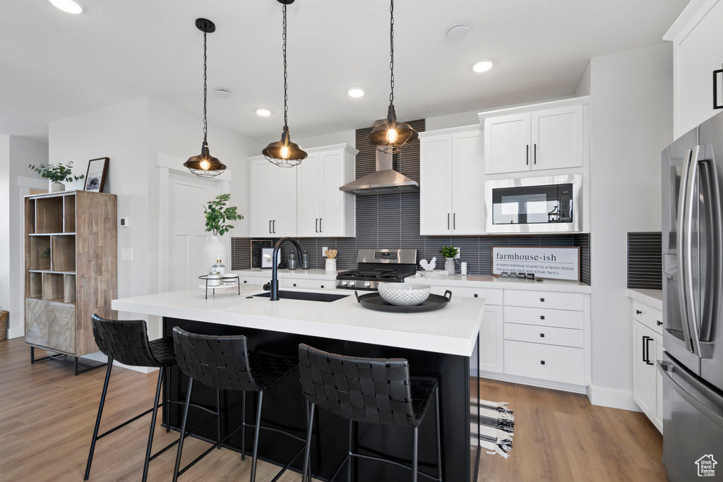 Kitchen with light hardwood / wood-style floors, range, decorative light fixtures, backsplash, and wall chimney range hood