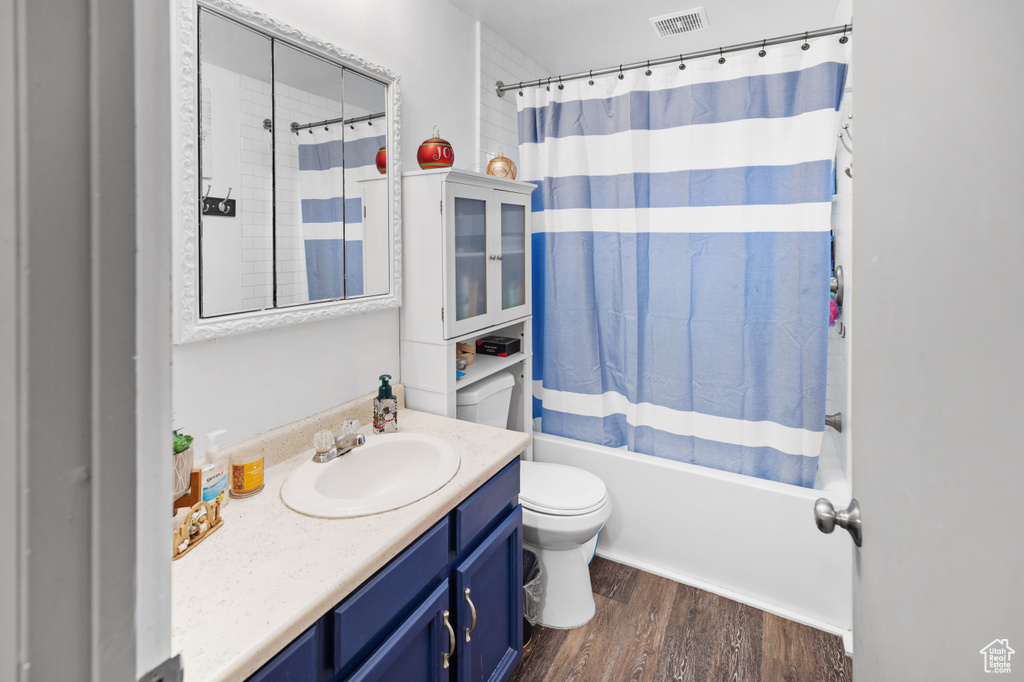 Full bathroom featuring wood-type flooring, toilet, large vanity, and shower / bathtub combination with curtain