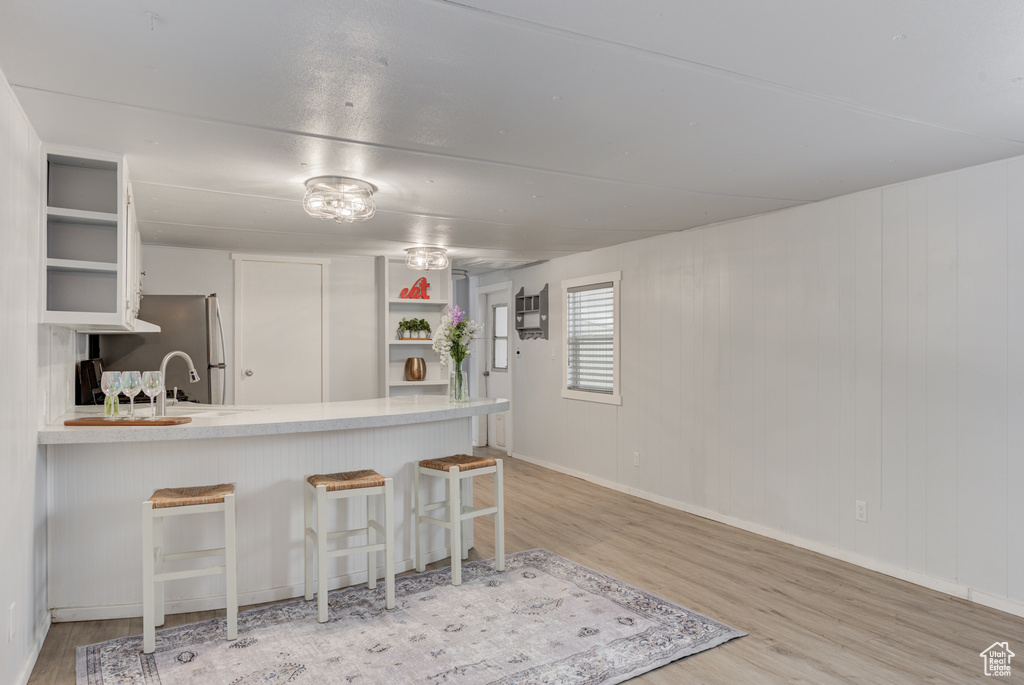 Kitchen with kitchen peninsula, a kitchen breakfast bar, white cabinets, stainless steel fridge, and light wood-type flooring