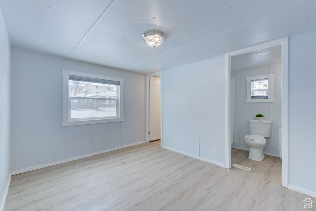 Unfurnished bedroom with ensuite bathroom and light hardwood / wood-style floors