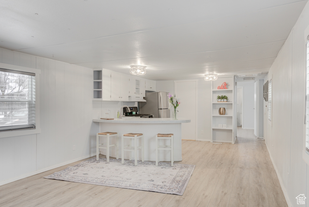 Kitchen featuring light wood-type flooring, stove, kitchen peninsula, and stainless steel fridge