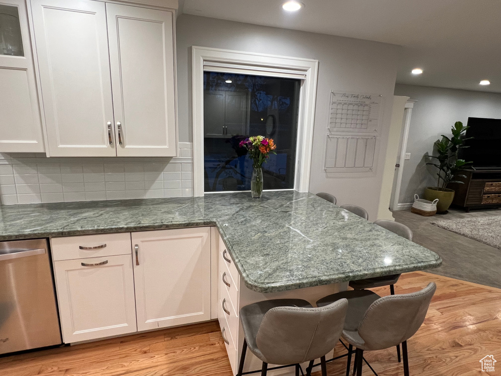 Kitchen featuring a kitchen bar, dishwasher, light wood-type flooring, tasteful backsplash, and white cabinetry