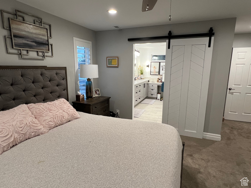 Carpeted bedroom featuring a barn door, connected bathroom, and ceiling fan
