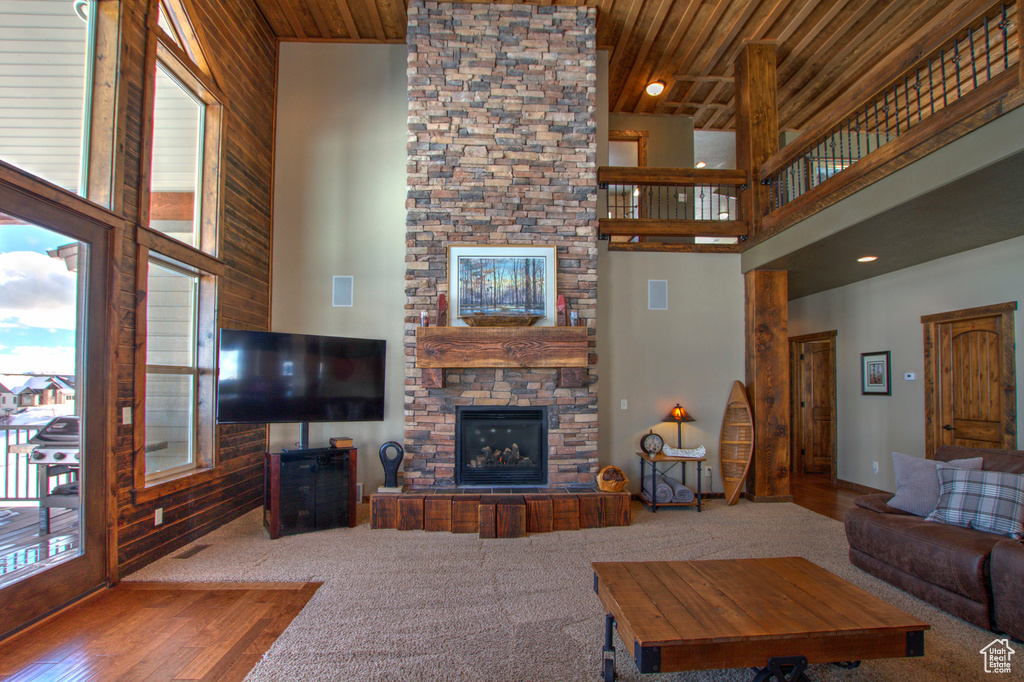 Carpeted living room with a stone fireplace, a healthy amount of sunlight, high vaulted ceiling, and wood ceiling