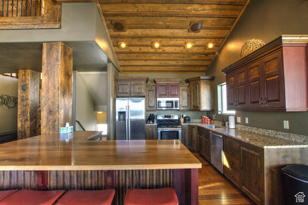 Kitchen with wooden ceiling, lofted ceiling, a breakfast bar, dark wood-type flooring, and stainless steel appliances