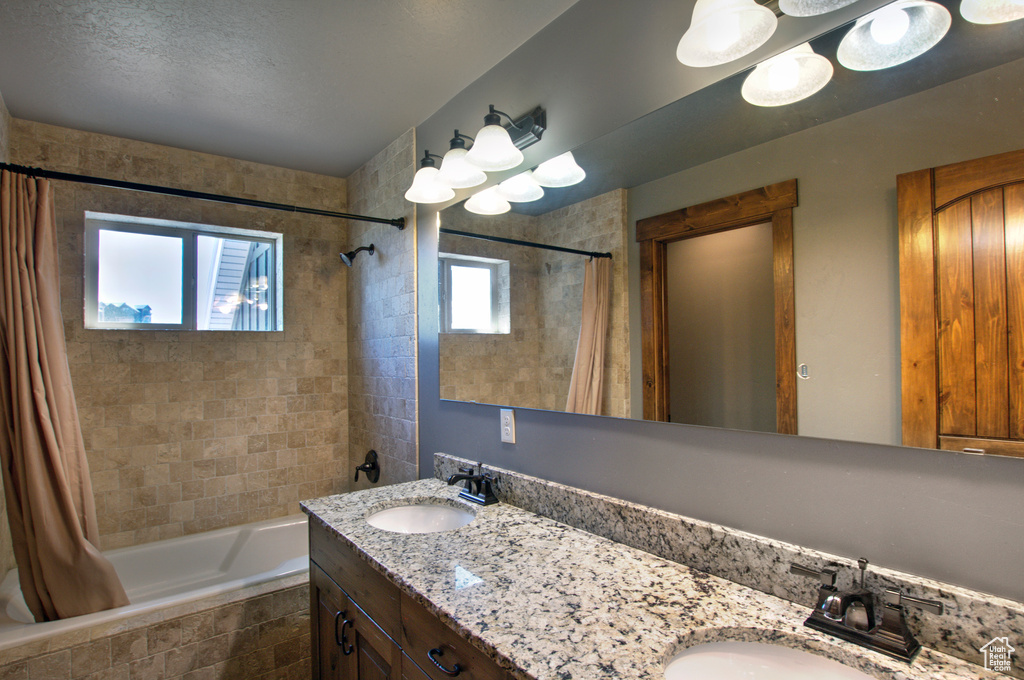 Bathroom with a textured ceiling, double sink vanity, and shower / bath combo