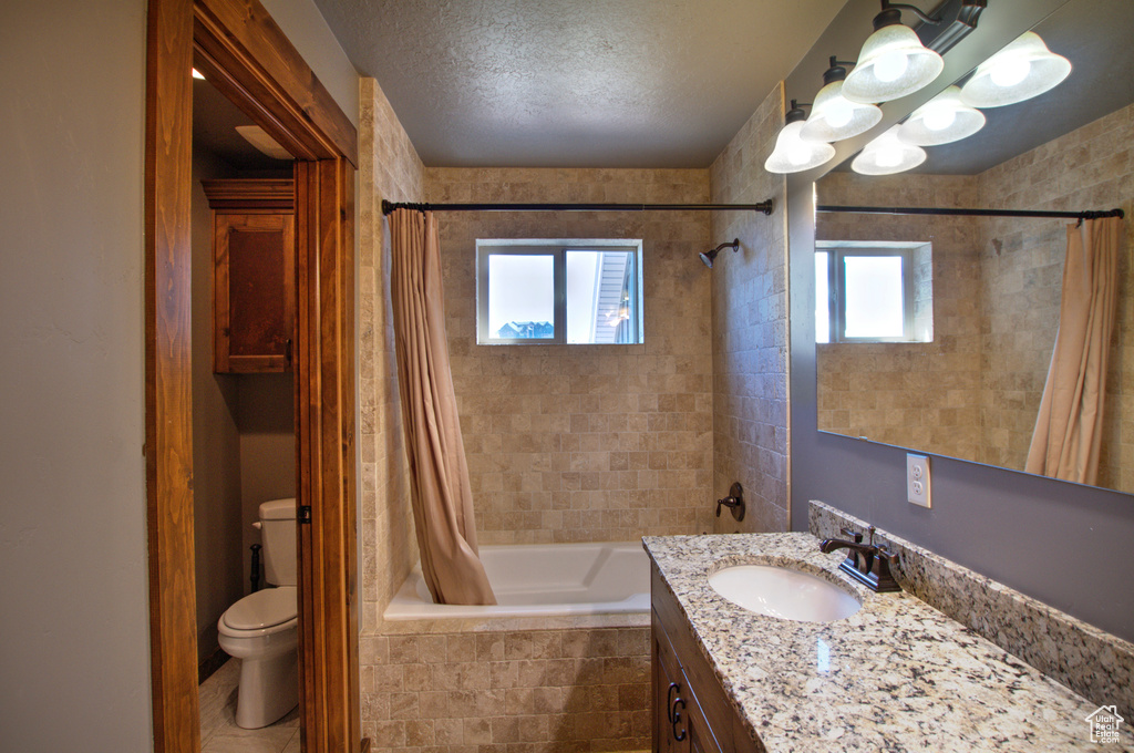 Full bathroom featuring toilet, shower / tub combo with curtain, large vanity, tile floors, and a textured ceiling