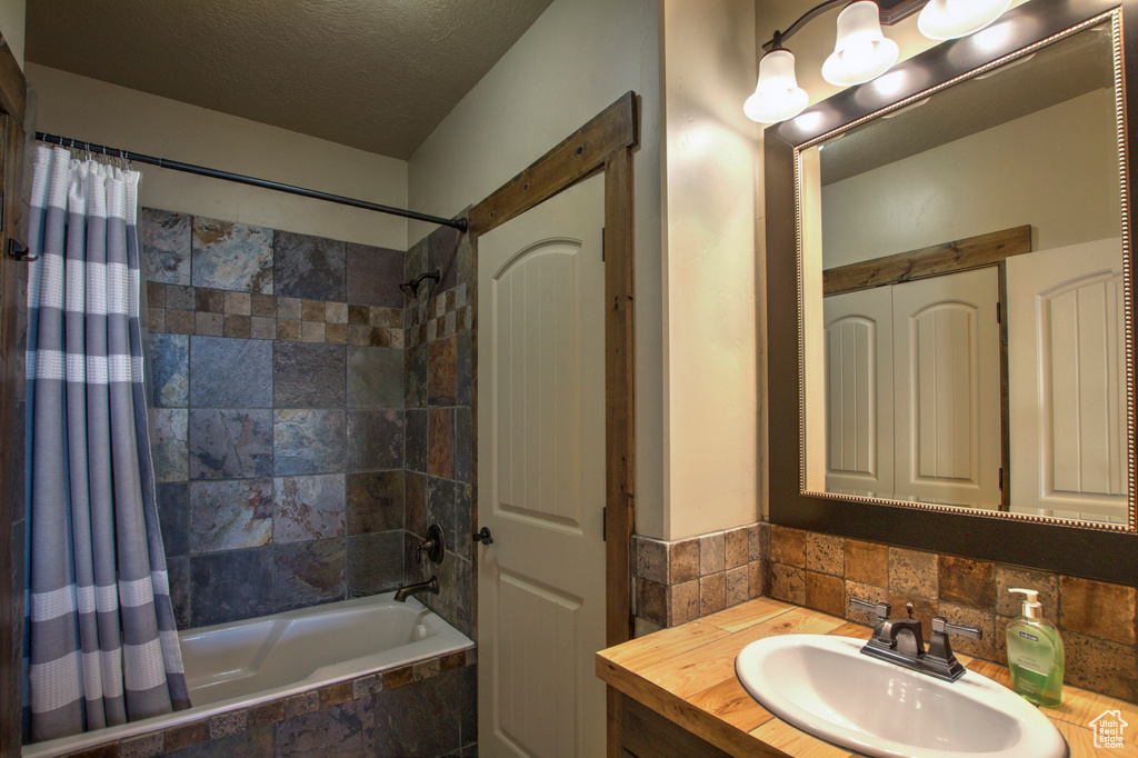 Bathroom with tasteful backsplash, oversized vanity, shower / tub combo, and a textured ceiling