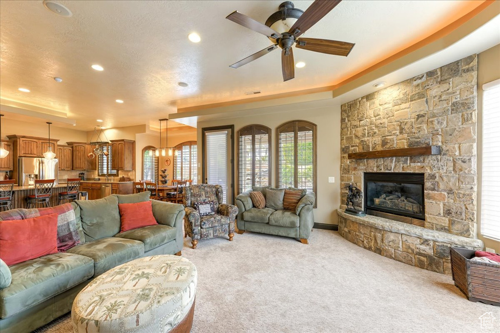 Living room featuring a tray ceiling, a fireplace, light colored carpet, and ceiling fan