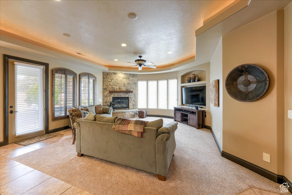 Living room featuring plenty of natural light, a stone fireplace, a tray ceiling, and ceiling fan