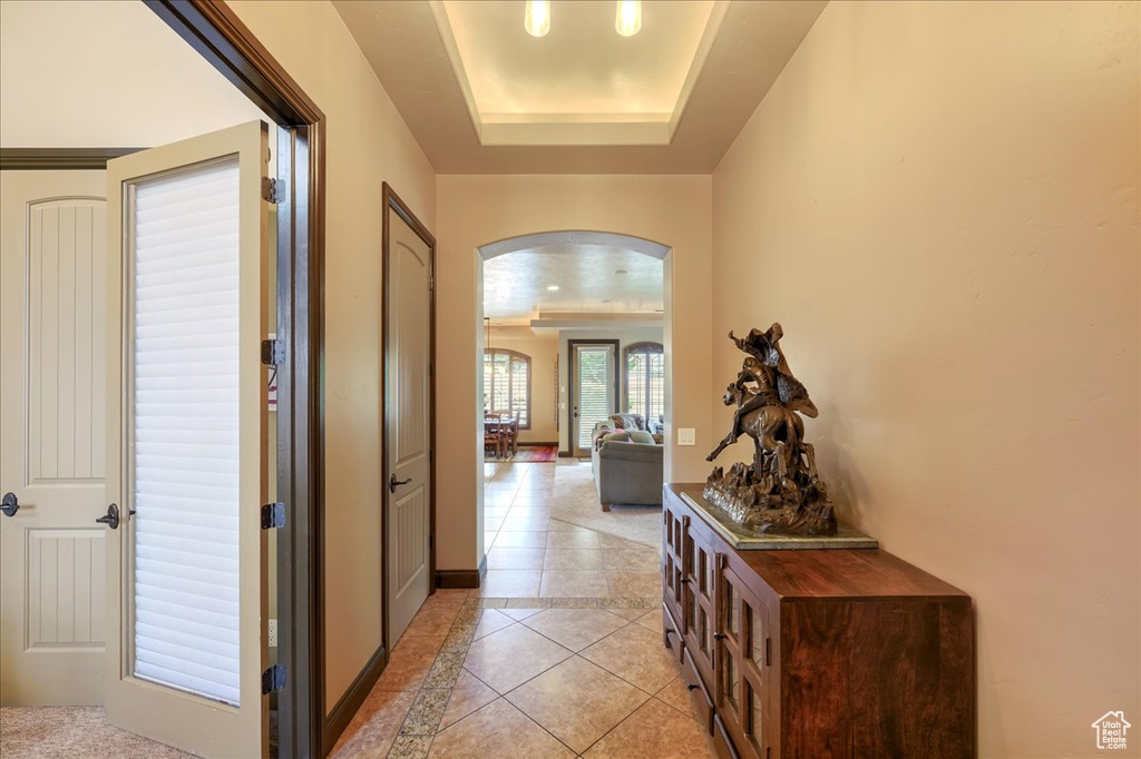 Hall with a tray ceiling and light tile flooring
