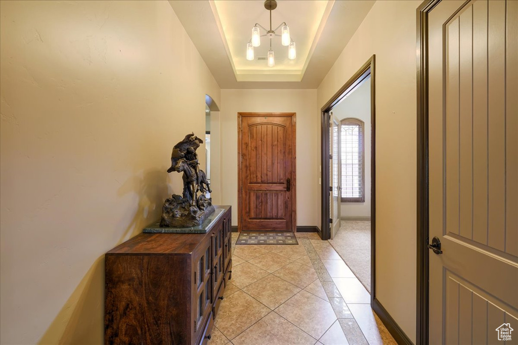 Foyer entrance with a chandelier, a tray ceiling, and light tile floors