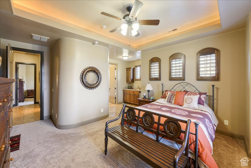 Bedroom featuring a raised ceiling, ensuite bathroom, light tile floors, and ceiling fan