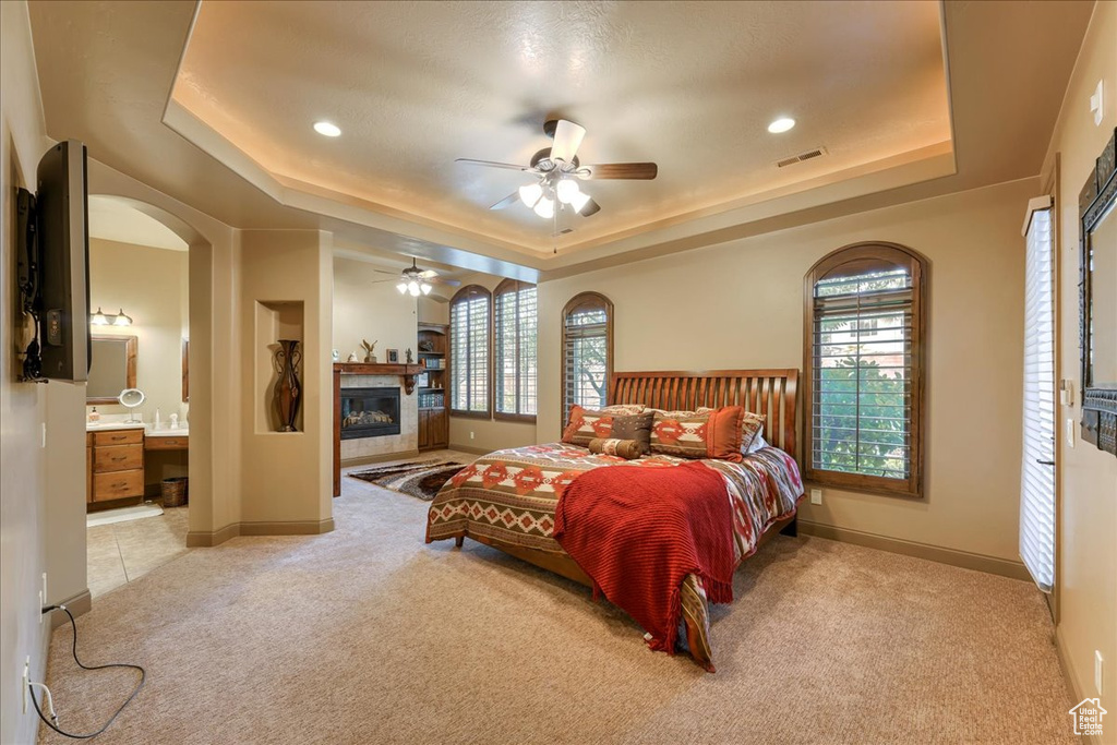 Bedroom featuring light carpet, ceiling fan, ensuite bathroom, and a raised ceiling