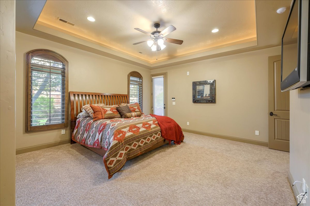 Carpeted bedroom featuring a raised ceiling and ceiling fan