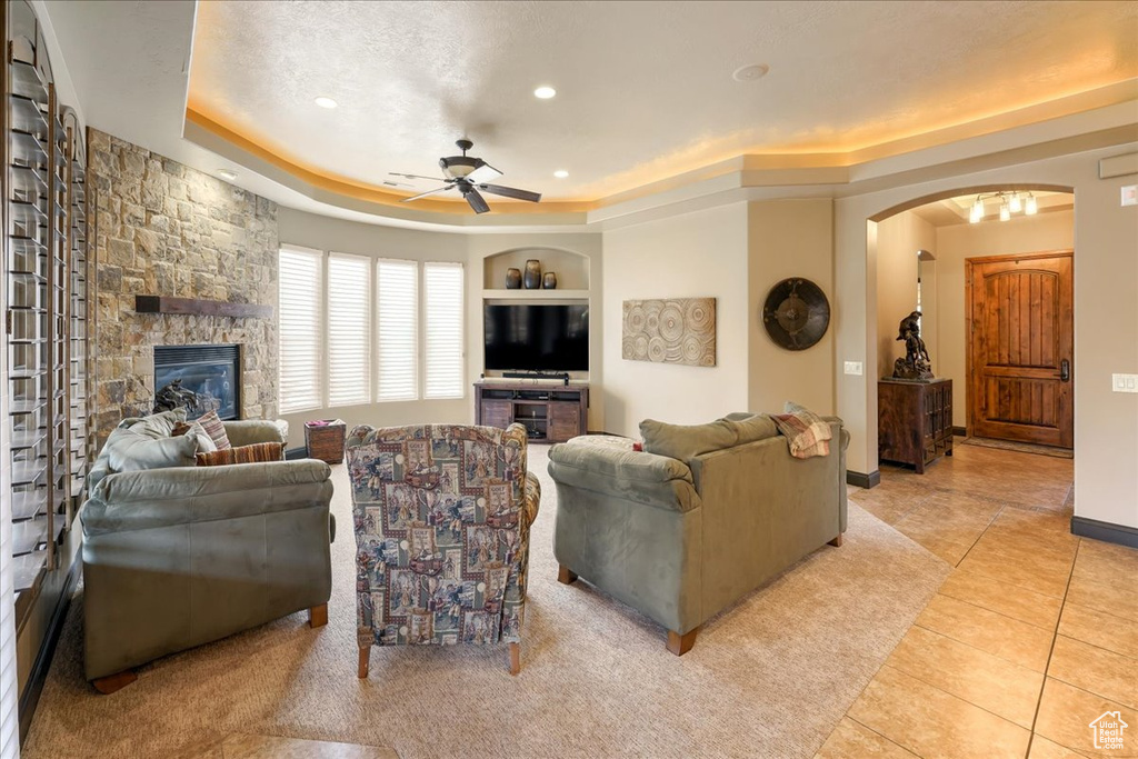 Living room with light tile flooring, ceiling fan, a fireplace, and a tray ceiling