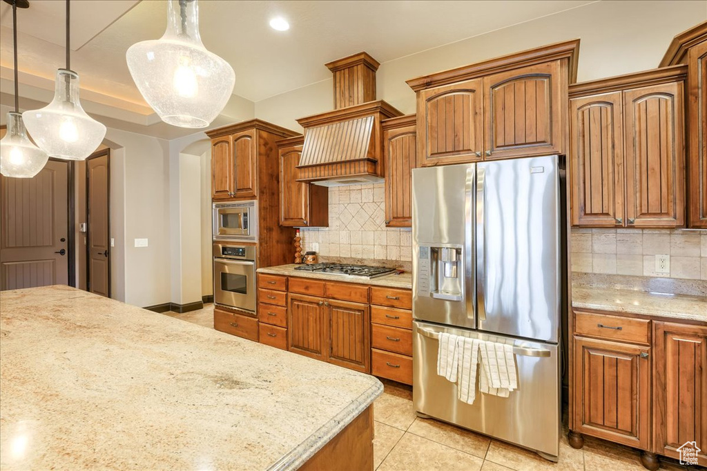 Kitchen with appliances with stainless steel finishes, light tile floors, decorative light fixtures, and backsplash
