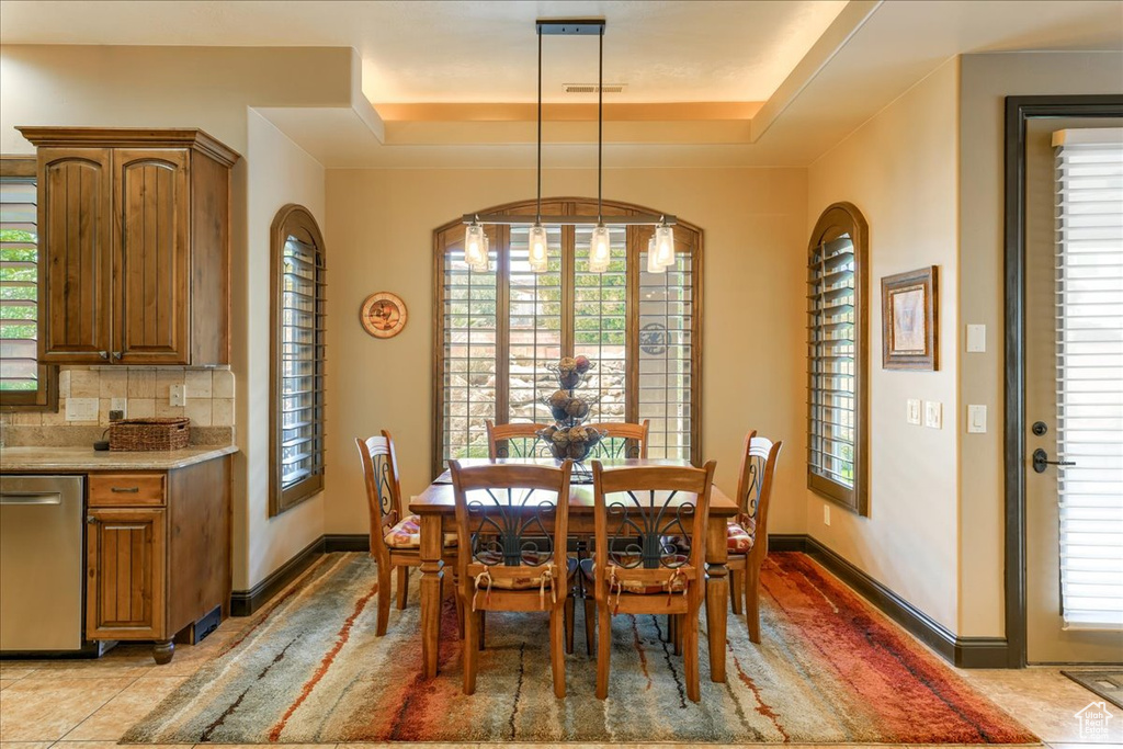Dining space featuring an inviting chandelier, light tile flooring, and a tray ceiling