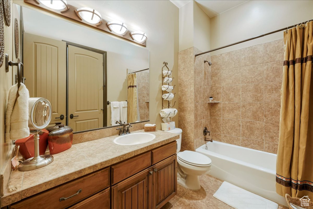 Full bathroom with toilet, vanity with extensive cabinet space, shower / bath combo, and tile flooring
