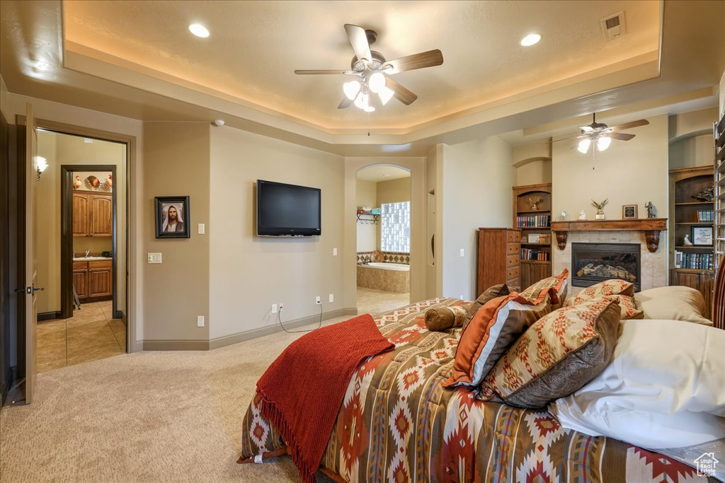 Bedroom featuring light carpet, a raised ceiling, ensuite bath, and ceiling fan