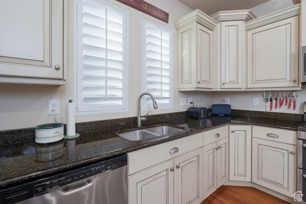 Kitchen featuring sink, stainless steel appliances, light hardwood / wood-style flooring, and dark stone countertops